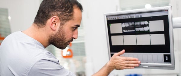 Manlig tandläkare tittar på röntgenbilder på skärm